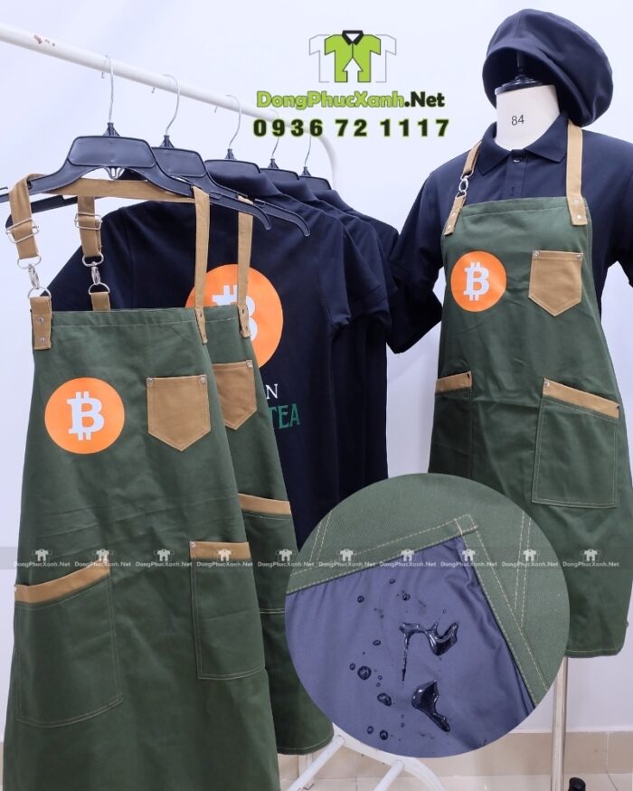 Bộ đồng phục quán cafe gồm áo thun đen có logo Bitcoin và tạp dề màu xanh rêu in logo Bit Coin Cafe & Tea.