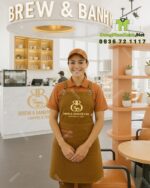 Tạp dề đồng phục màu nâu vàng mộc mạc dành cho nhân viên quán cà phê, in logo Brew & Bánh Mì Cafe.