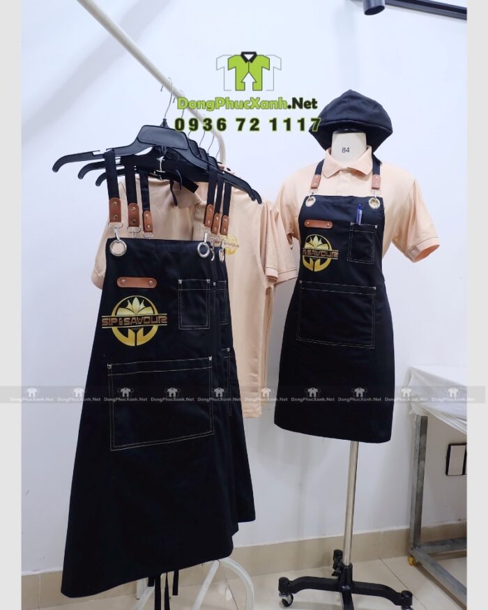 Bộ đồng phục gồm áo thun màu be và tạp dề đen, in logo Sip & Savour nổi bật