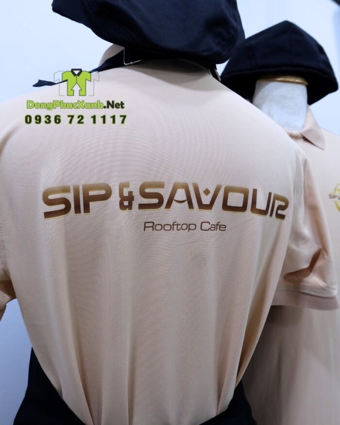 Bộ đồng phục gồm áo thun màu be và tạp dề đen, in logo Sip & Savour nổi bật