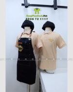 Bộ đồng phục gồm áo thun màu be và tạp dề đen, in logo Sip & Savour nổi bật