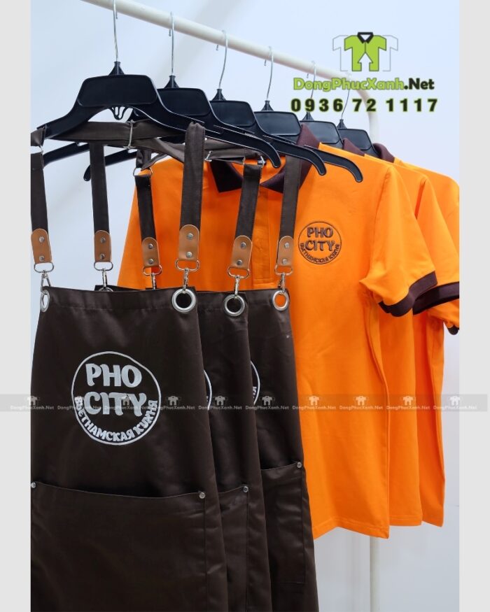 Bộ đồng phục quán ăn Pho City gồm áo thun cam và tạp dề nâu in logo nổi bật