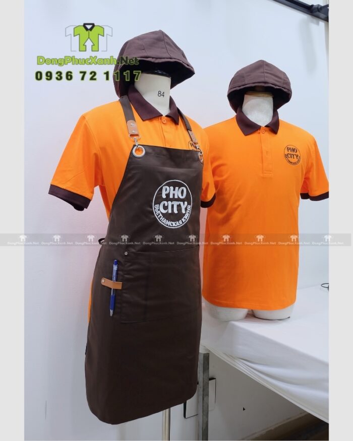 Bộ đồng phục quán ăn Pho City gồm áo thun cam và tạp dề nâu in logo nổi bật