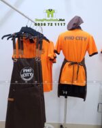Bộ đồng phục quán ăn Pho City gồm áo thun cam và tạp dề nâu in logo nổi bật