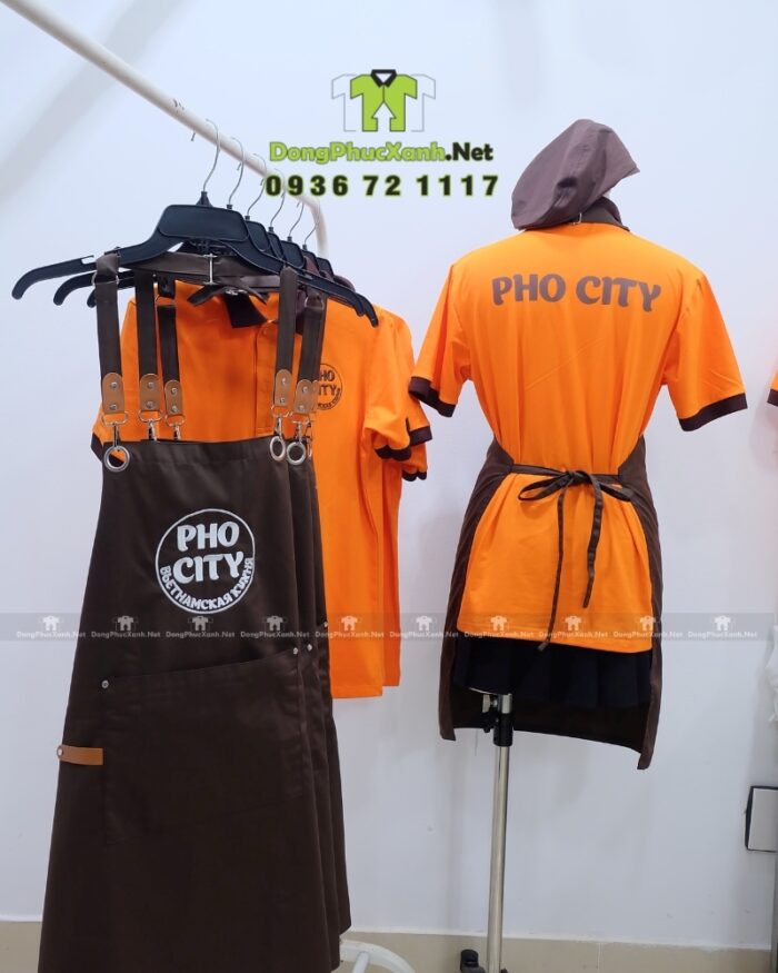 Bộ đồng phục quán ăn Pho City gồm áo thun cam và tạp dề nâu in logo nổi bật