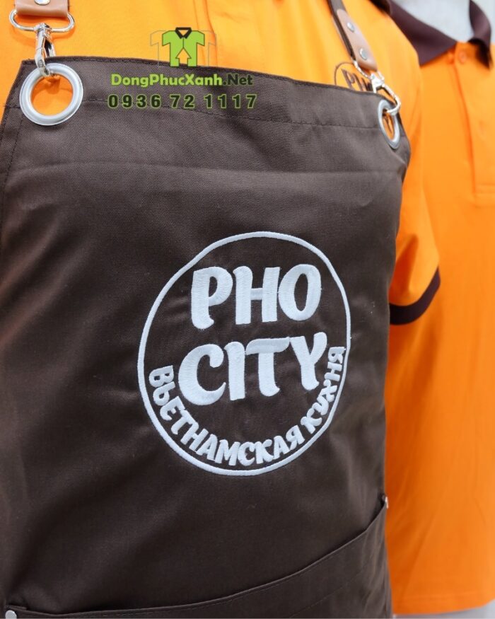 Bộ đồng phục quán ăn Pho City gồm áo thun cam và tạp dề nâu in logo nổi bật