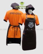 Bộ đồng phục quán ăn Pho City gồm áo thun cam và tạp dề nâu in logo nổi bật