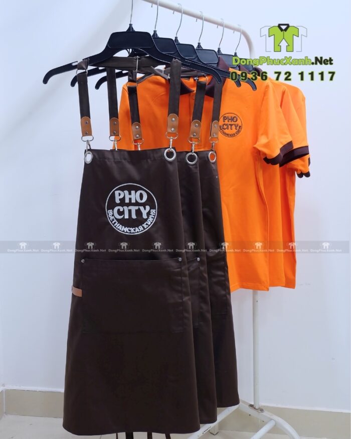 Bộ đồng phục quán ăn Pho City gồm áo thun cam và tạp dề nâu in logo nổi bật
