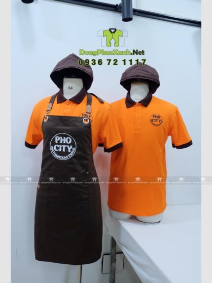 Bộ đồng phục quán ăn Pho City gồm áo thun cam và tạp dề nâu in logo nổi bật